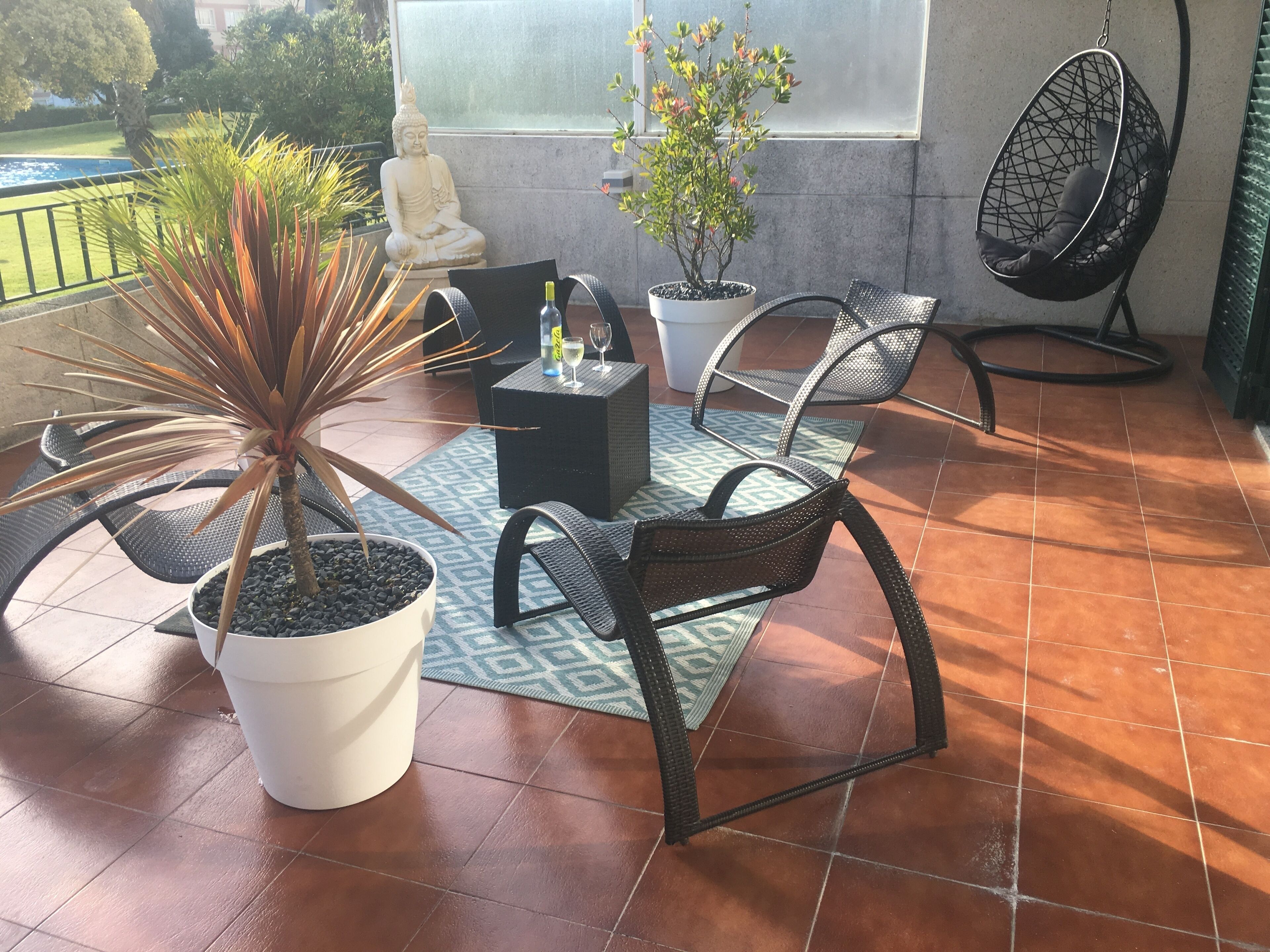 Un patio con una estatua de Buda, plantas en macetas, mobiliario exterior y un ventilador.