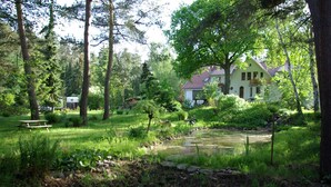 A house surrounded by a lush garden with a small pond, picnic table, and a covered area. - Ferienwohnung Seerose (Bleckede)