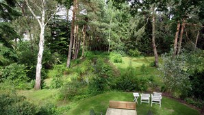A garden with a wooden table and four chairs, surrounded by dense greenery and trees. - Ferienwohnung Seerose (Bleckede)