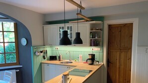 A kitchen with a central island, white cabinets, a black hanging light, and a wooden door. - Ferienwohnung Seerose (Bleckede)