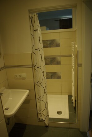 A bathroom with a shower, a sink, and a tiled floor. - Ferienwohnung Seerose (Bleckede)