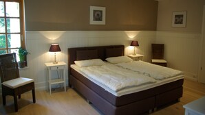 A bedroom with a large bed, two bedside lamps, a chair, and a potted plant. - Ferienwohnung Seerose (Bleckede)