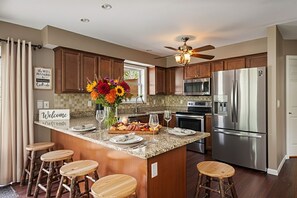 A kitchen with wooden cabinets, a stainless steel refrigerator, a ceiling fan, and a welcome sign.