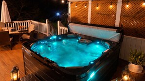 Un jacuzzi con cubierta de madera, rodeado de luces colgantes y una valla blanca.
