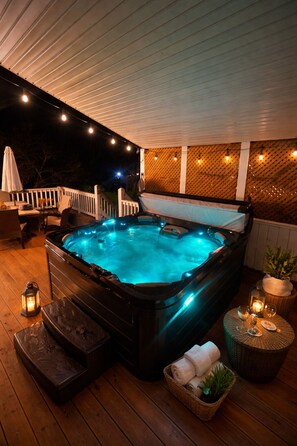 Un bain à remous avec une terrasse en bois, entouré de guirlandes lumineuses et d’une clôture blanche.