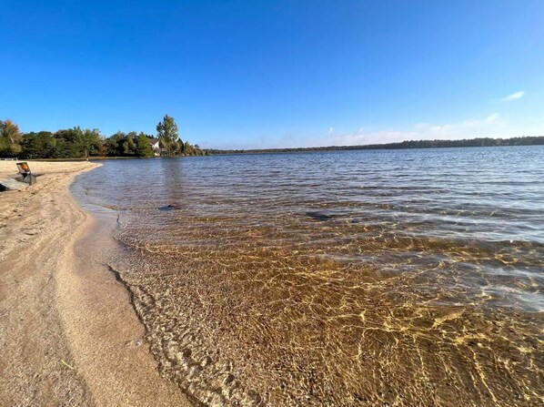 A beach with clear water, a sandy shore, and trees in the background.