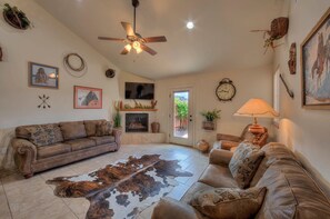 A living room with a brown leather sofa, a ceiling fan, a fireplace, and a cowhide rug.