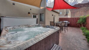 A hot tub in a backyard with a wooden deck, a table with chairs, and a red canopy.