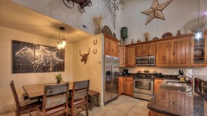 A kitchen with wooden cabinets, a stainless steel refrigerator, a microwave, and a stove. There is a dining table with chairs and a wall-mounted light fixture.