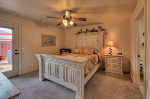 A bedroom with a large bed, a ceiling fan, a nightstand with a lamp, and a framed picture on the wall.