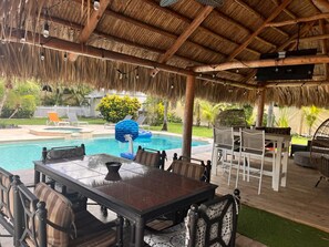 An outdoor pool area with a covered patio, lounge chairs, and a dining table.