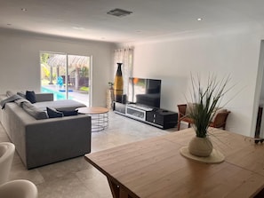 A modern living room with a sofa, TV, and a dining table with a plant.