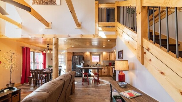 A spacious living area with a wooden staircase, a kitchen in the background, and a cozy seating area. - Just Built New Cabin In the Valley Year Round Access, The Barn Owl (Maggie Valley)
