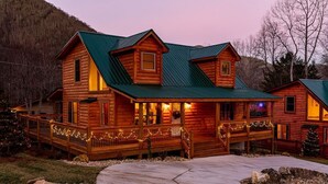 A log cabin with a green roof, a porch with string lights, and a Christmas tree. - Just Built New Cabin In the Valley Year Round Access, The Barn Owl (Maggie Valley)