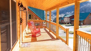 A wooden deck with a covered porch, red rocking chairs, and a view of a mountain landscape. - Just Built New Cabin In the Valley Year Round Access, The Barn Owl (Maggie Valley)