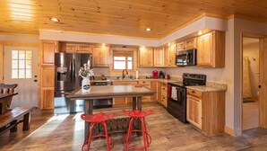 A spacious kitchen with wooden cabinets, a large island, and red bar stools. - Just Built New Cabin In the Valley Year Round Access, The Barn Owl (Maggie Valley)