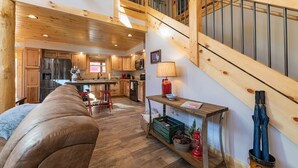 A spacious living area with a wooden staircase, a kitchen with wooden cabinets, and a cozy seating area. - Just Built New Cabin In the Valley Year Round Access, The Barn Owl (Maggie Valley)