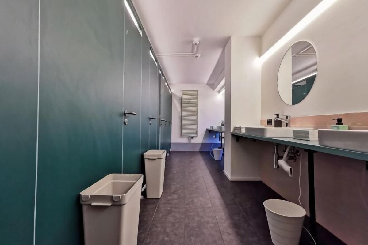 A modern bathroom with a long corridor, individual stalls, a sink area, and a mirror.