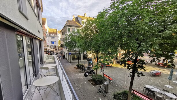 A balcony with outdoor seating, a tree, and a cobblestone street below. - Green Marmot Capsule Hotel Zurich (Zürich)