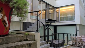 A modern building with a staircase leading to an upper level, outdoor seating area, and a large planter with greenery. - Green Marmot Capsule Hotel Zurich (Zürich)