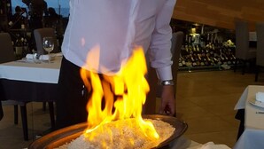 Un chef cocina arroz con llamas sobre una mesa en un restaurante.