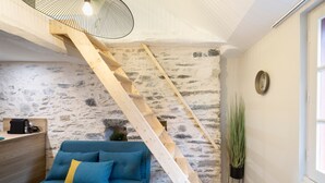 A room with a blue sofa, a wooden ladder, a stone wall, and a potted plant.