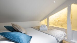A bedroom with a sloped ceiling, a brick wall, and a large window.