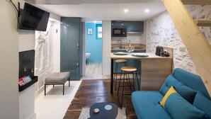 A compact living space with a kitchenette, a sofa, a small table, and a TV mounted on the wall.