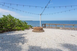 A gravel area with a stone fire pit, a wooden deck, and string lights. - DOLPHINS🐬,BEACH step away,WATER VIEW,SUNRISE, FREE WIFI,FREE PARKING,POOLS #611 (Ruskin)