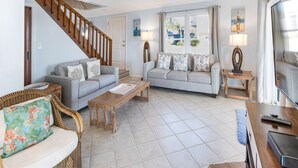 A living room with a staircase, two sofas, a coffee table, and a TV. - Oceanview Retreat | Just Steps from the Beach (Tybee Island)