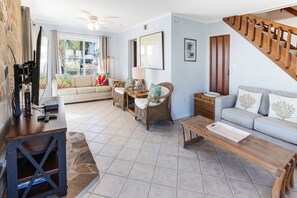 Un salón amplio con un sofá, dos sillones de mimbre, una mesa de centro y un mueble de televisión con control remoto.
