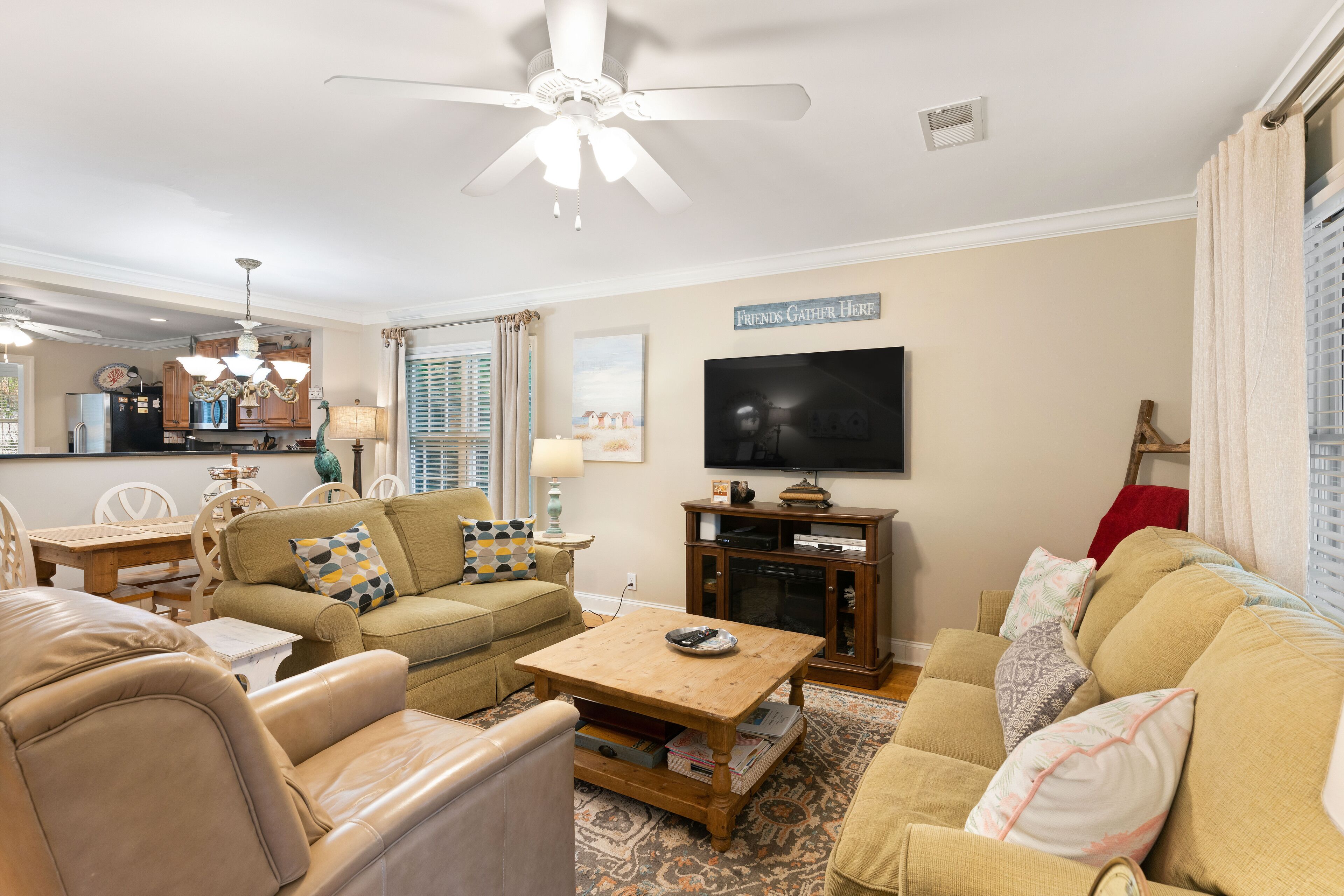 Ein Wohnzimmer mit Deckenventilator, Fernseher und einem Schild mit der Aufschrift 'Friends Gather Here'.