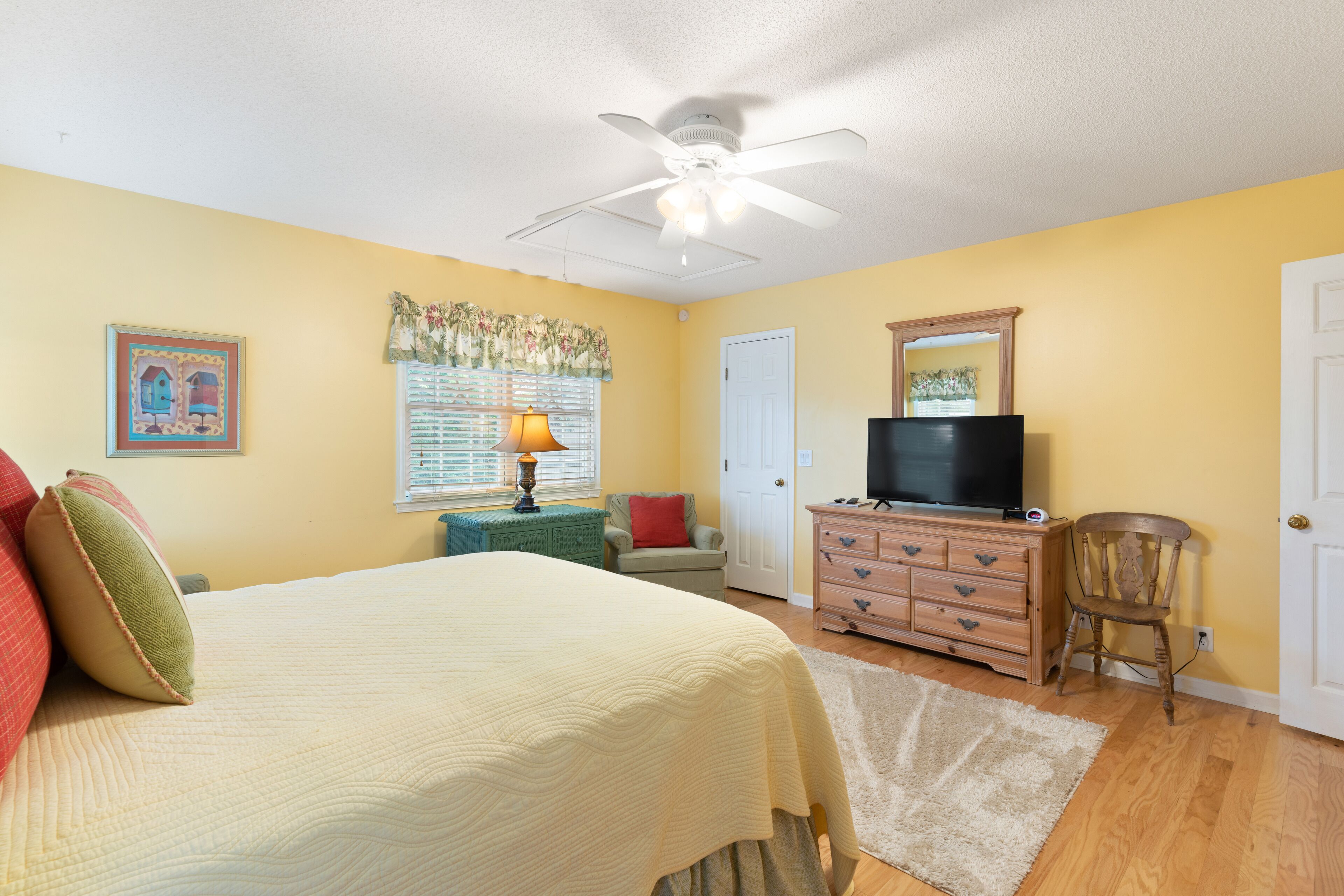 A bedroom with a bed, dresser, television, and a ceiling fan.