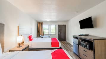 A hotel room with two beds, a TV, a desk with a microwave, and a window with curtains.
