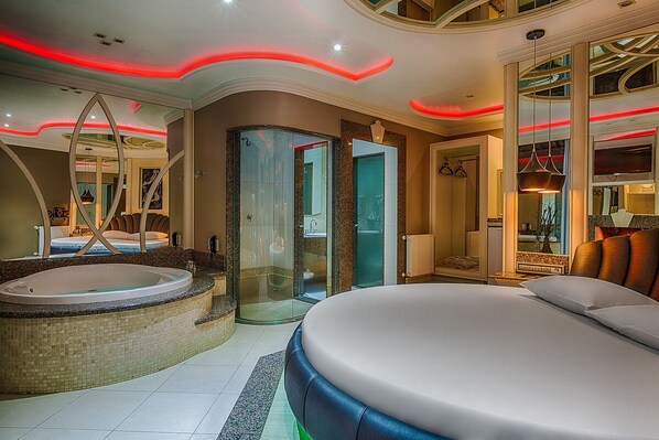 Habitación de hotel moderna con una cama grande, un jacuzzi y zona de ducha con paredes de vidrio.