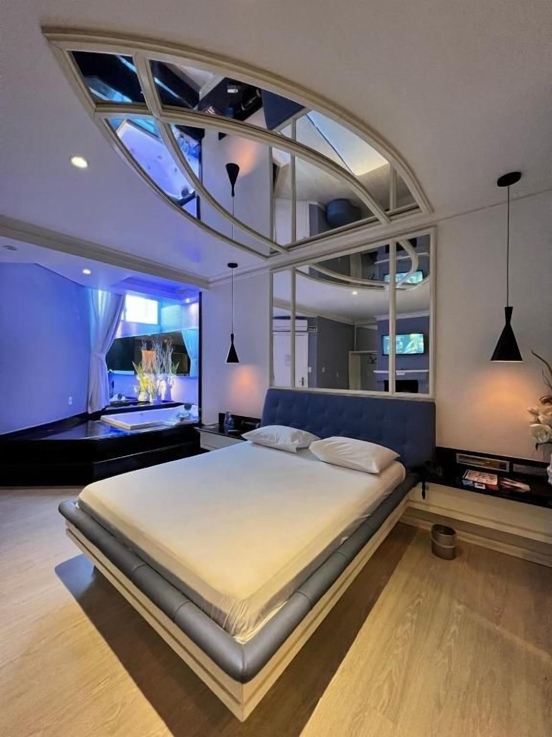 Quarto moderno com uma cama grande, claraboia e televisão sobre um suporte.