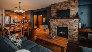 Una sala de estar con chimenea de piedra, un comedor con muebles de madera y un televisor montado en la pared.