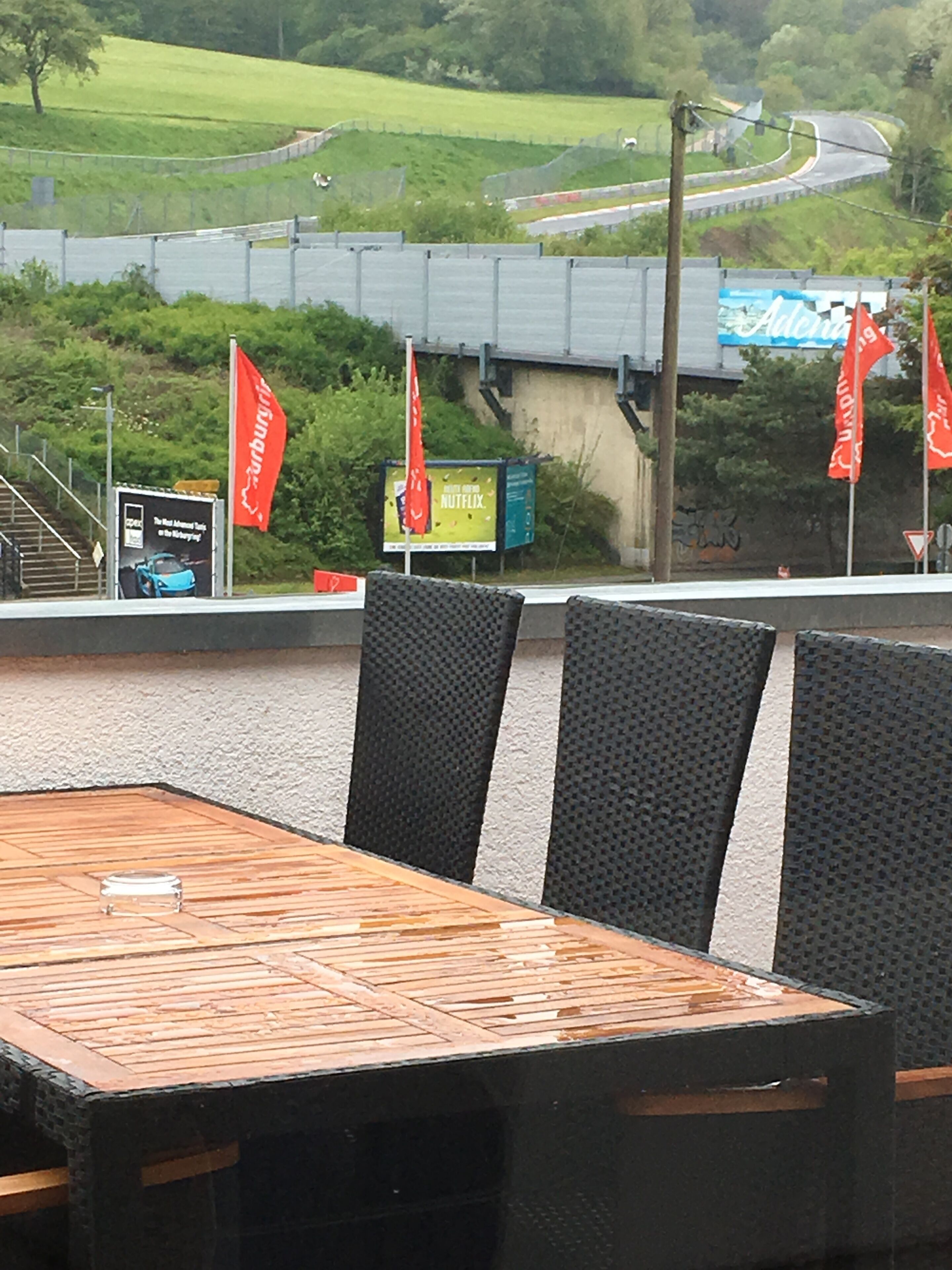 Un espace extérieur aménagé avec une table et des chaises, donnant sur une route et sur un espace verdoyant.