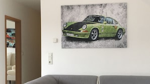 A living room with a grey sofa and a wall-mounted artwork of a green Porsche 911. - Nringrooms Exit-Breidscheid (Adenau)