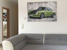 Un salón con un sofá gris y una obra de arte en la pared de un Porsche 911 verde.