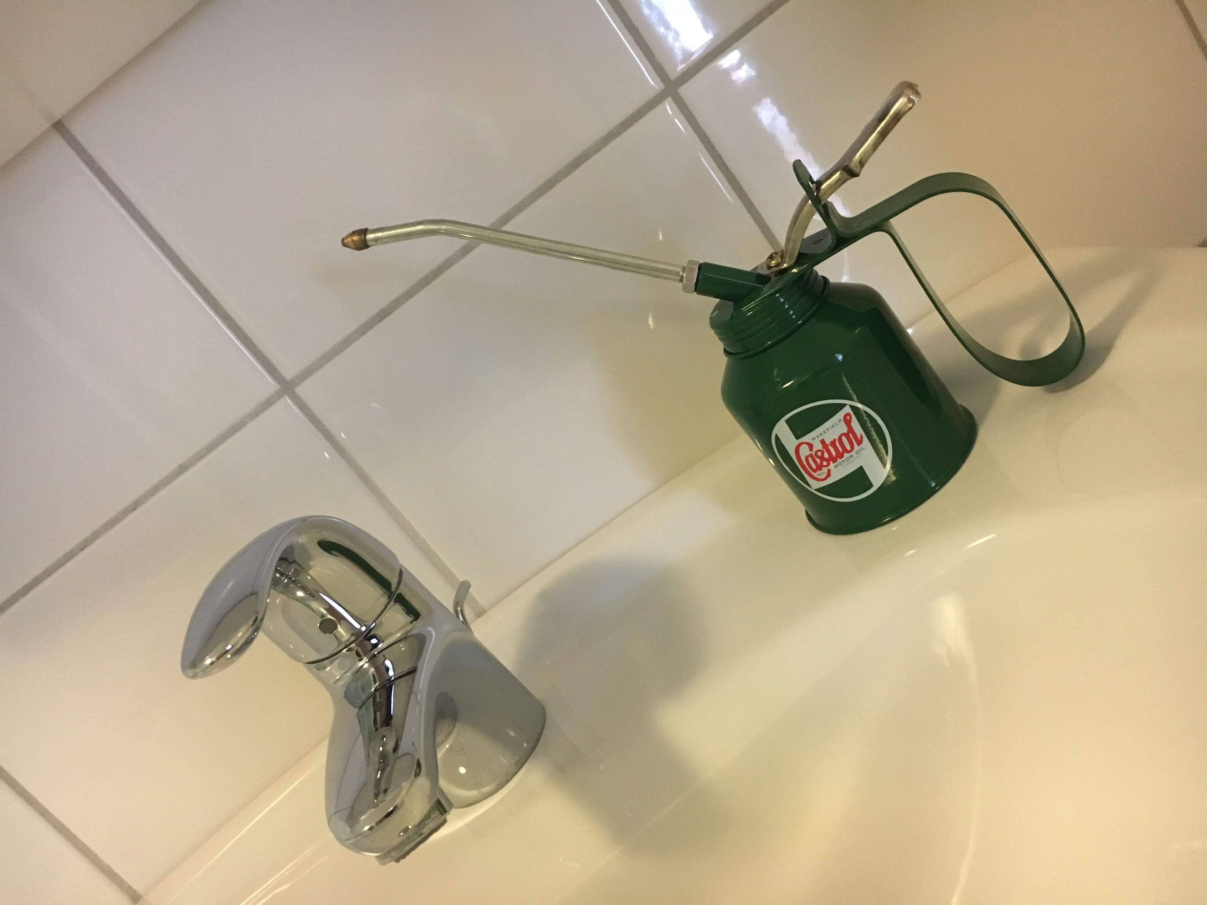 A bathroom with a sink, a green Castrol motor oil bottle, and a faucet.