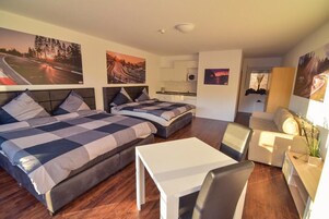 Una habitación de hotel moderna con dos camas, un pequeño comedor y una kitchenette.