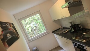A compact kitchen with a window, a sink, a stove, and a trash bin. - Nringrooms Exit-Breidscheid (Adenau)