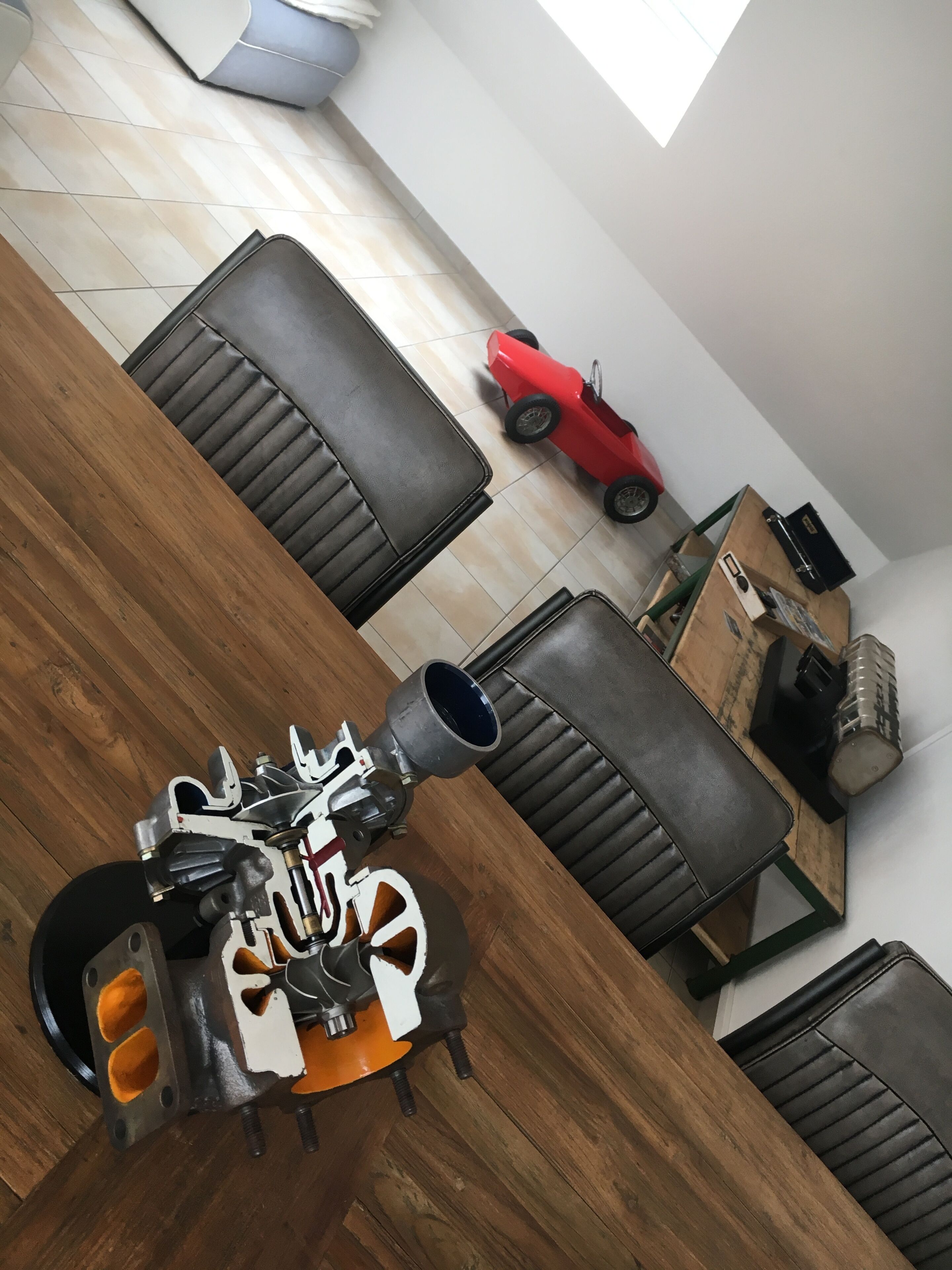 Een eetgedeelte met een houten tafel, zwarte leren stoelen en een rode kinderauto op de vloer.