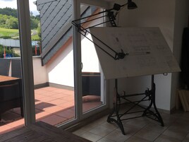 Una habitación con un ventanal grande, un ventilador de techo y un atril con un dibujo.