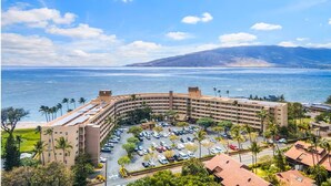 A hotel with a curved building, a parking lot, and a view of the ocean. - Amazing Ocean/Beach Front, Pool Side, Ground Floor Remodeled 2 Bdr 2 Bath Condo  (Kihei)