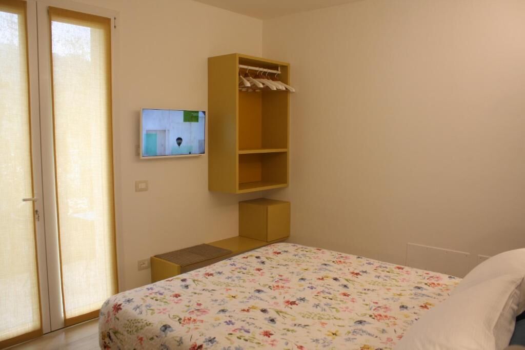 Ein Schlafzimmer mit einem Bett, einem Holzschrank, einem an der Wand montierten Fernseher und einer Schiebetür aus Glas.