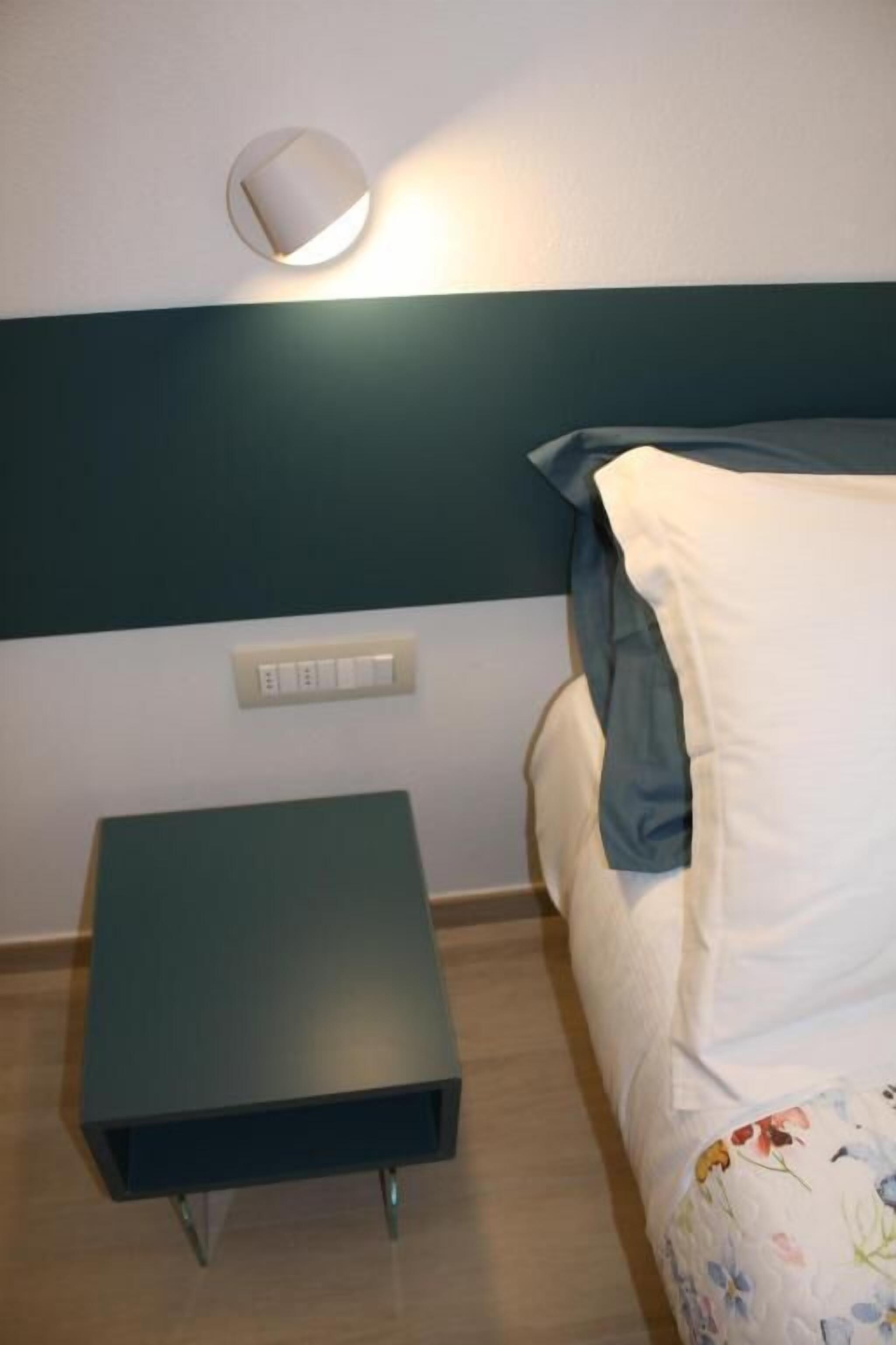 A bed with a floral duvet, a bedside table, and a wall-mounted light fixture.