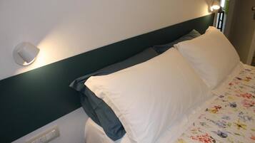 Una cama bien hecha con ropa de cama blanca y gris, un cabecero verde y una lámpara fijada a la pared.