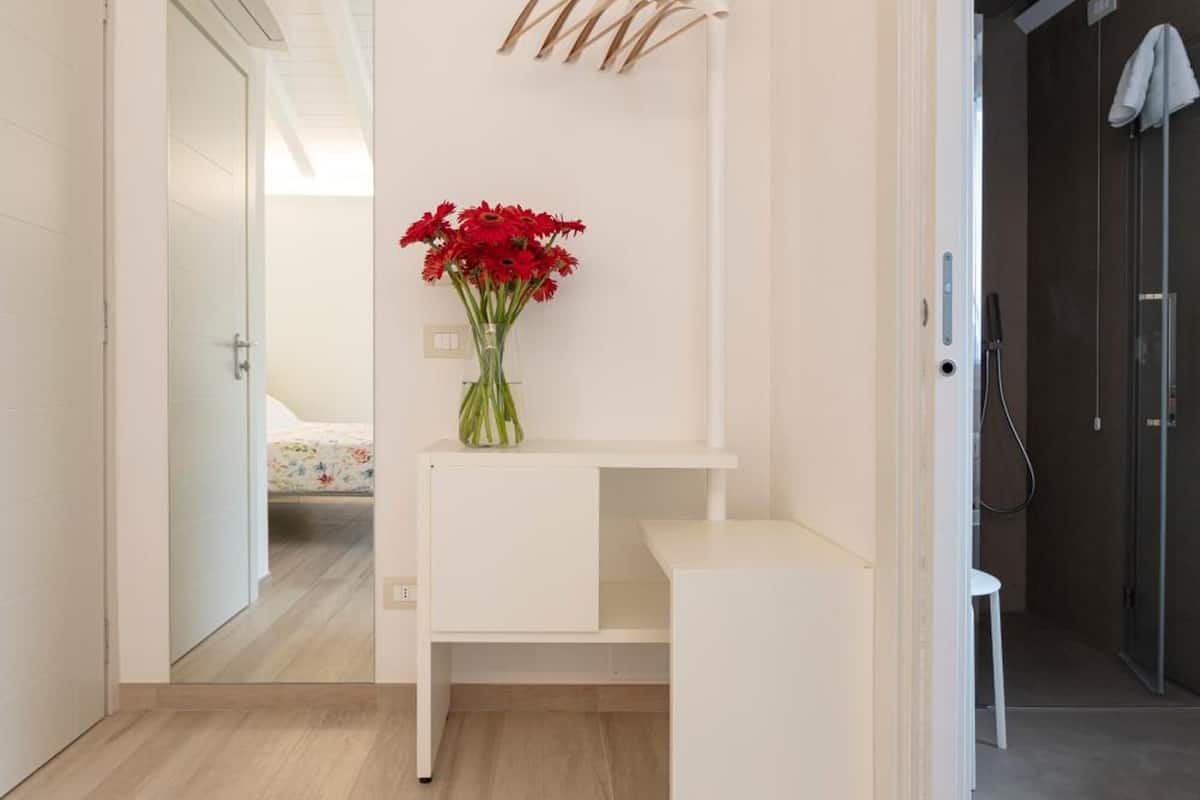 Une salle de bain moderne avec un meuble-lavabo blanc, un porte-serviettes suspendu et un vase rempli de fleurs rouges.